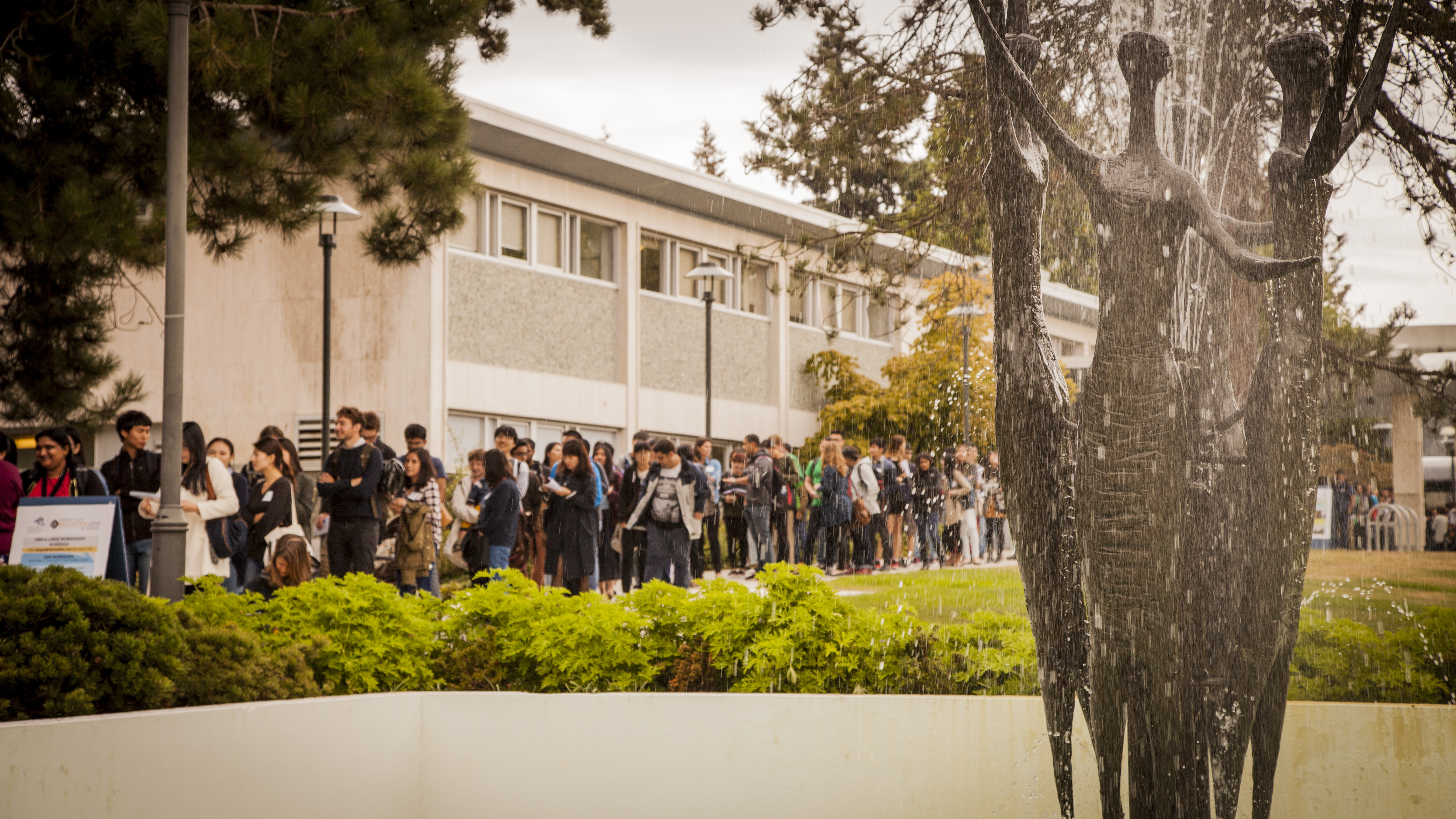 Students line up in front of the University Centre, behind the Trancendence fountain.